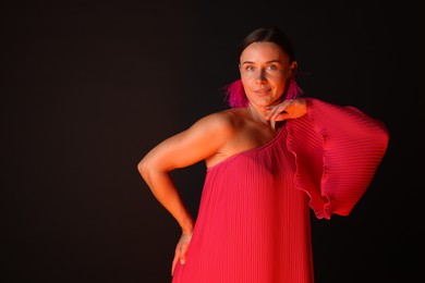Photo of Beautiful woman wearing fur earrings in neon lights against black background. Space for text
