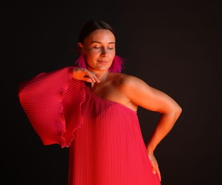 Photo of Beautiful woman wearing fur earrings in neon lights against black background