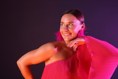 Photo of Smiling woman wearing fur earrings in neon lights against purple background