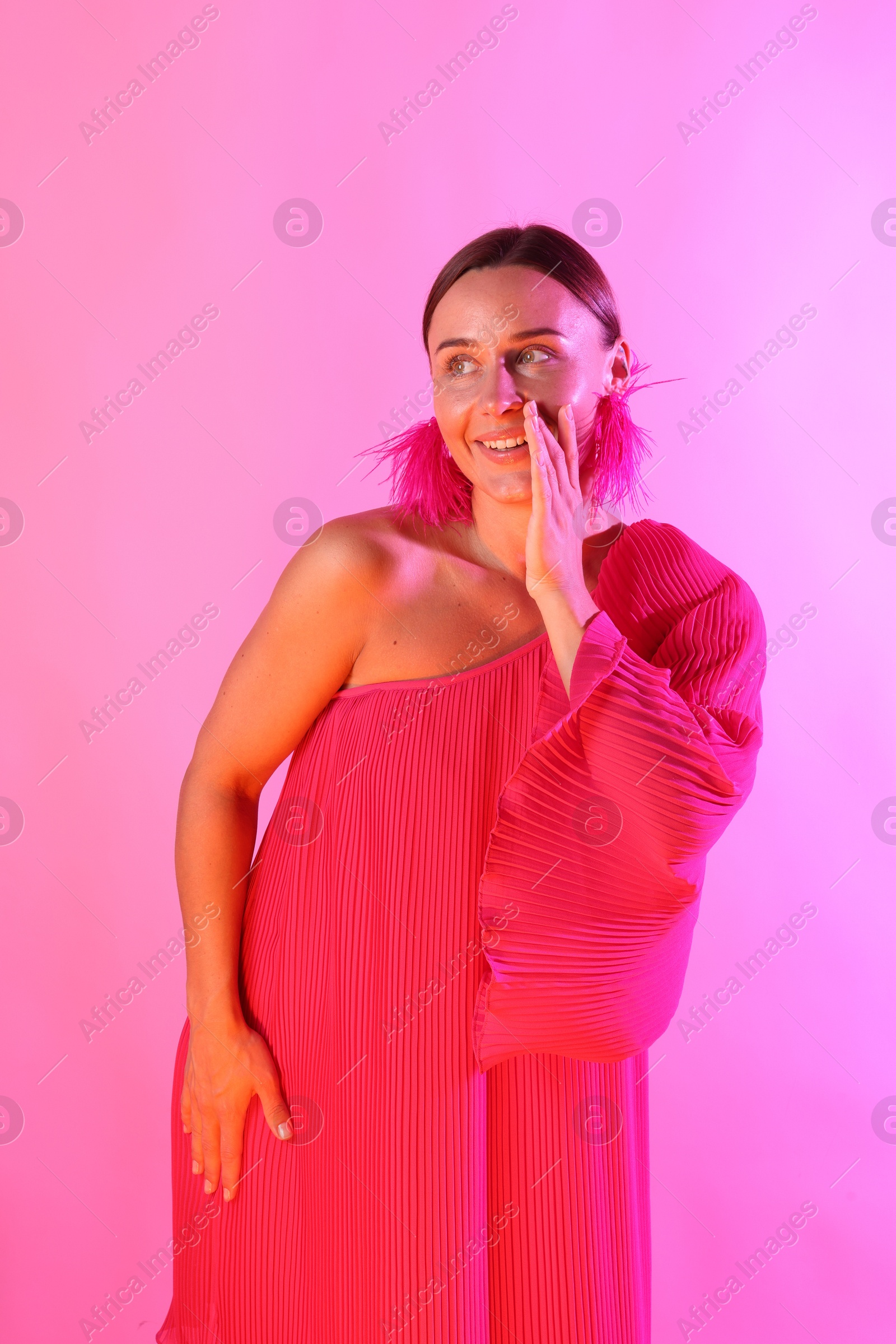 Smiling woman wearing fur earrings in neon lights against pink background Photo of Smiling woman wearing fur earrings in neon lights against pink background