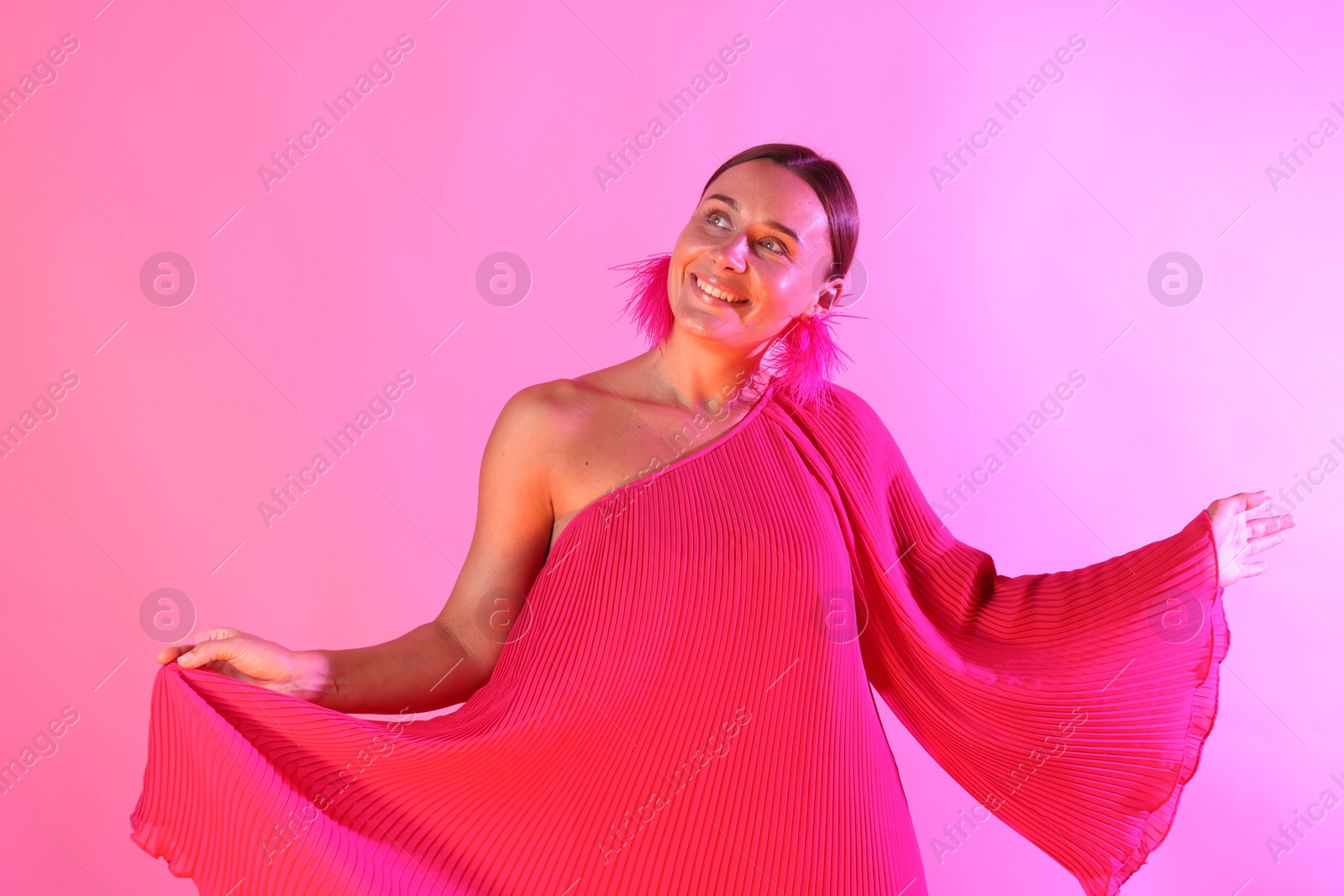 Smiling woman wearing fur earrings in neon lights against pink background Photo of Smiling woman wearing fur earrings in neon lights against pink background