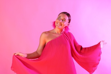 Photo of Smiling woman wearing fur earrings in neon lights against pink background