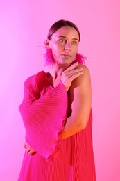 Photo of Beautiful woman wearing fur earrings in neon lights against pink background