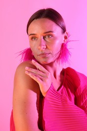 Photo of Beautiful woman wearing fur earrings in neon lights against pink background