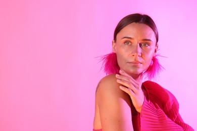 Photo of Beautiful woman wearing fur earrings in neon lights against pink background. Space for text