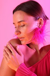 Photo of Beautiful woman wearing fur earrings in neon lights against pink background
