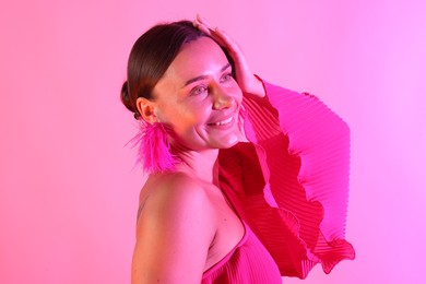 Photo of Smiling woman wearing fur earrings in neon lights against pink background