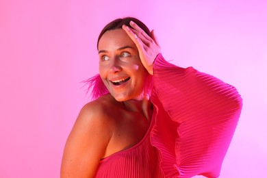 Photo of Happy woman wearing fur earrings in neon lights against pink background