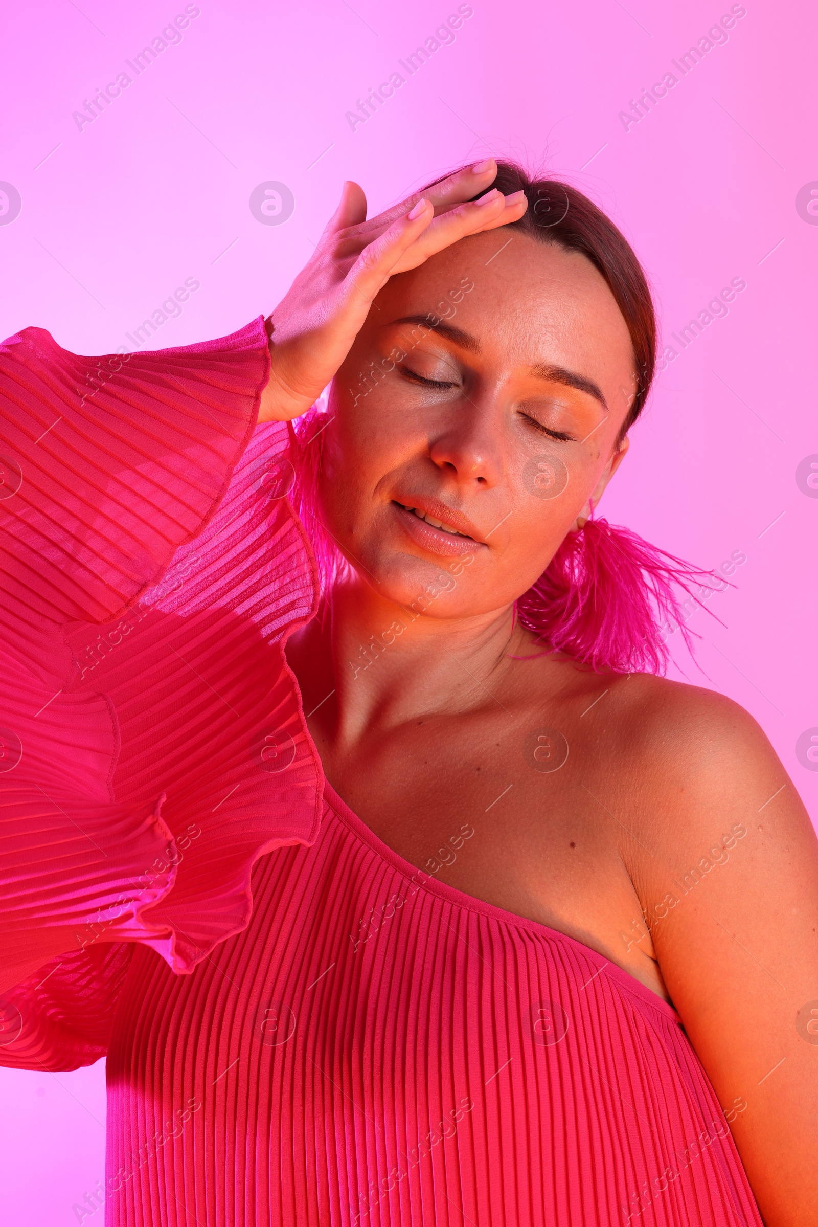 Beautiful woman wearing fur earrings in neon lights against pink background Photo of Beautiful woman wearing fur earrings in neon lights against pink background