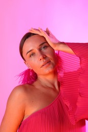 Photo of Portrait of beautiful woman wearing fur earrings in neon lights against pink background