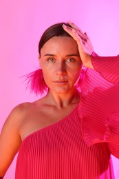 Photo of Portrait of beautiful woman wearing fur earrings in neon lights against pink background