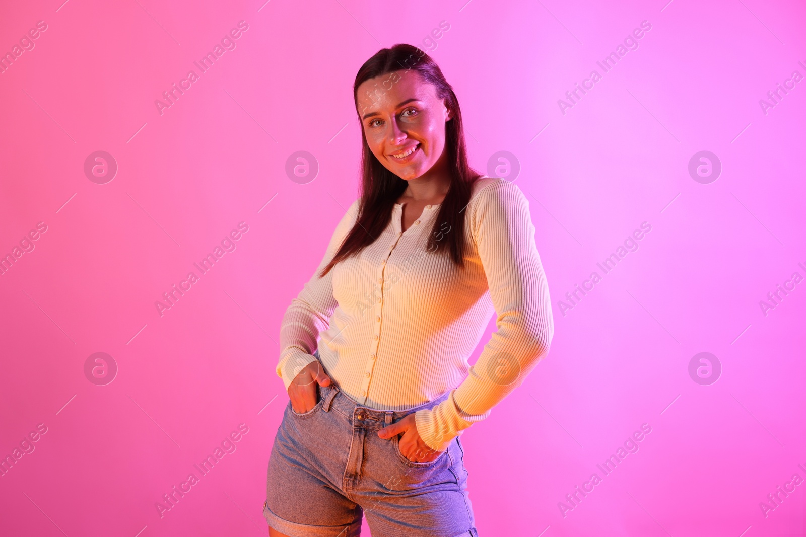 Smiling woman in neon lights against pink background Photo of Smiling woman in neon lights against pink background