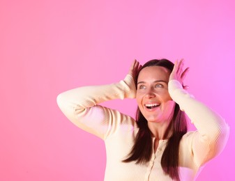 Photo of Smiling woman in neon lights against pink background. Space for text