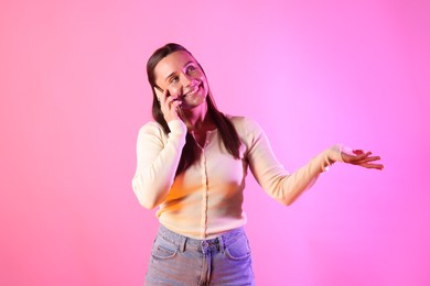 Photo of Smiling woman talking by smartphone in neon lights against pink background