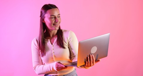 Photo of Smiling woman with laptop in neon lights against pink background