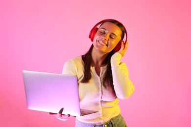 Photo of Smiling woman in headphones with laptop in neon lights against pink background