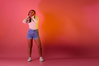Photo of Smiling woman in headphones listening to music in neon lights against pink background. Space for text