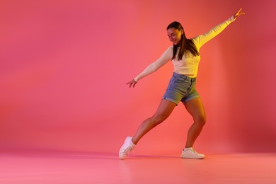 Photo of Smiling woman dancing in neon lights against pink background. Space for text