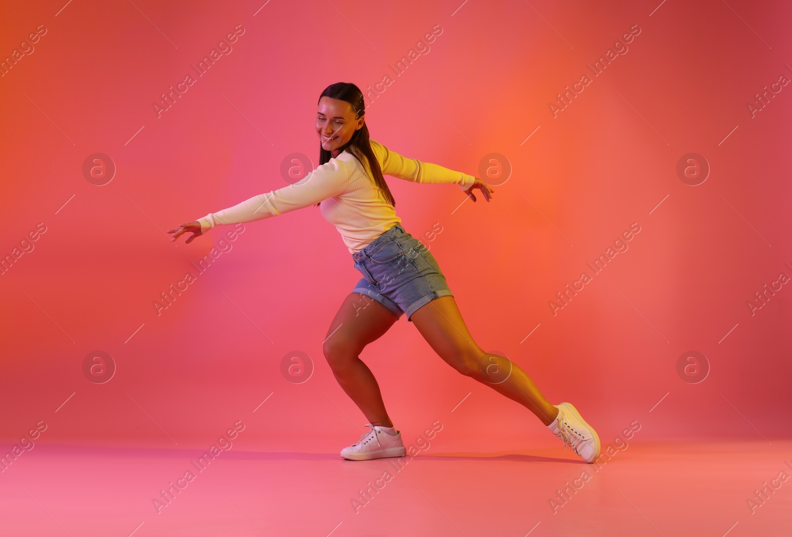 Smiling woman dancing in neon lights against pink background Photo of Smiling woman dancing in neon lights against pink background