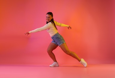 Photo of Smiling woman dancing in neon lights against pink background