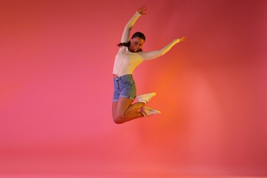 Photo of Smiling woman jumping in neon lights against pink background