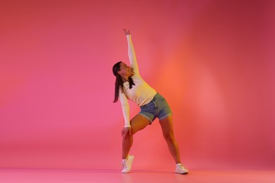 Photo of Smiling woman dancing in neon lights against pink background