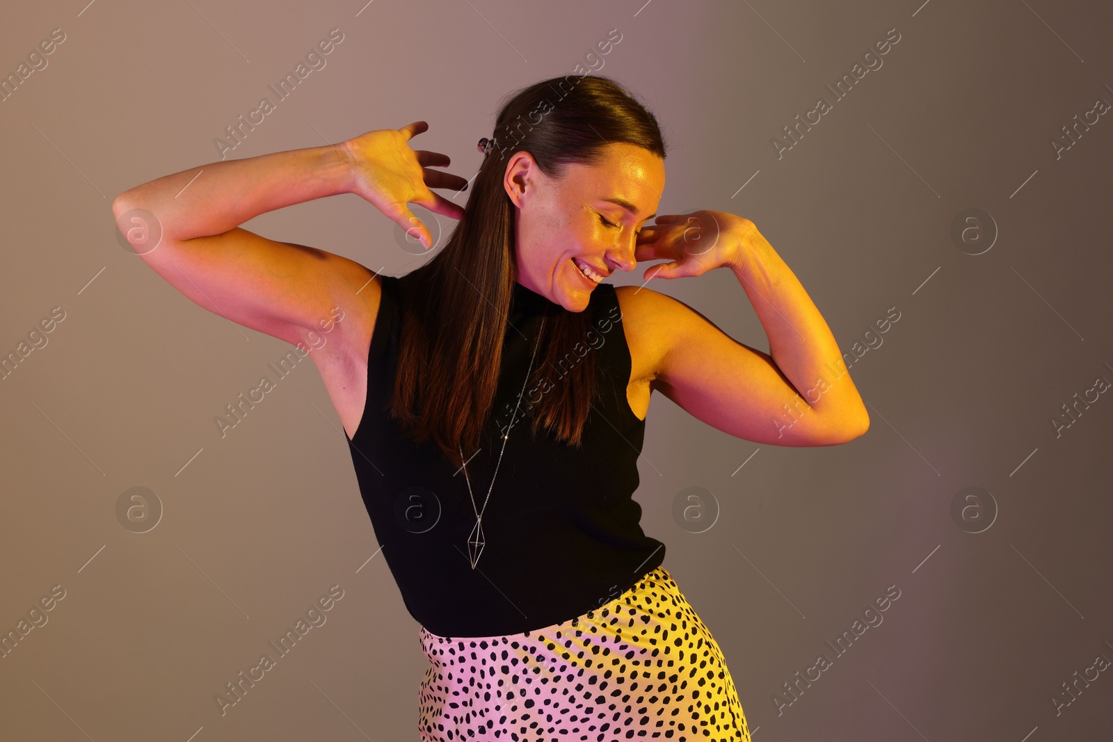 Smiling woman dancing in neon lights against grey background Photo of Smiling woman dancing in neon lights against grey background