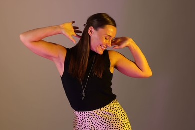 Photo of Smiling woman dancing in neon lights against grey background