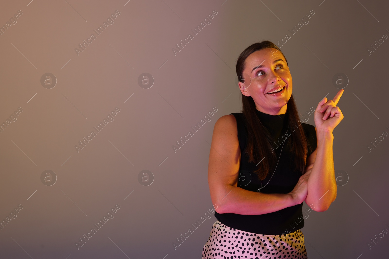 Photo of Happy woman pointing at something in neon lights against grey background. Space for text