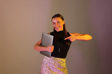Photo of Happy woman pointing at laptop in neon lights against grey background