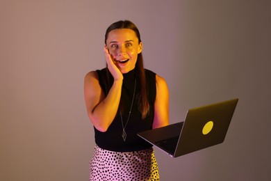 Photo of Emotional woman with laptop in neon lights against grey background