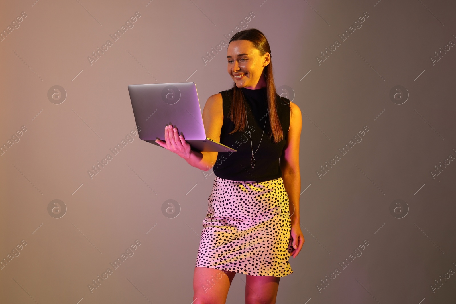 Happy woman with laptop in neon lights against grey background Photo of Happy woman with laptop in neon lights against grey background