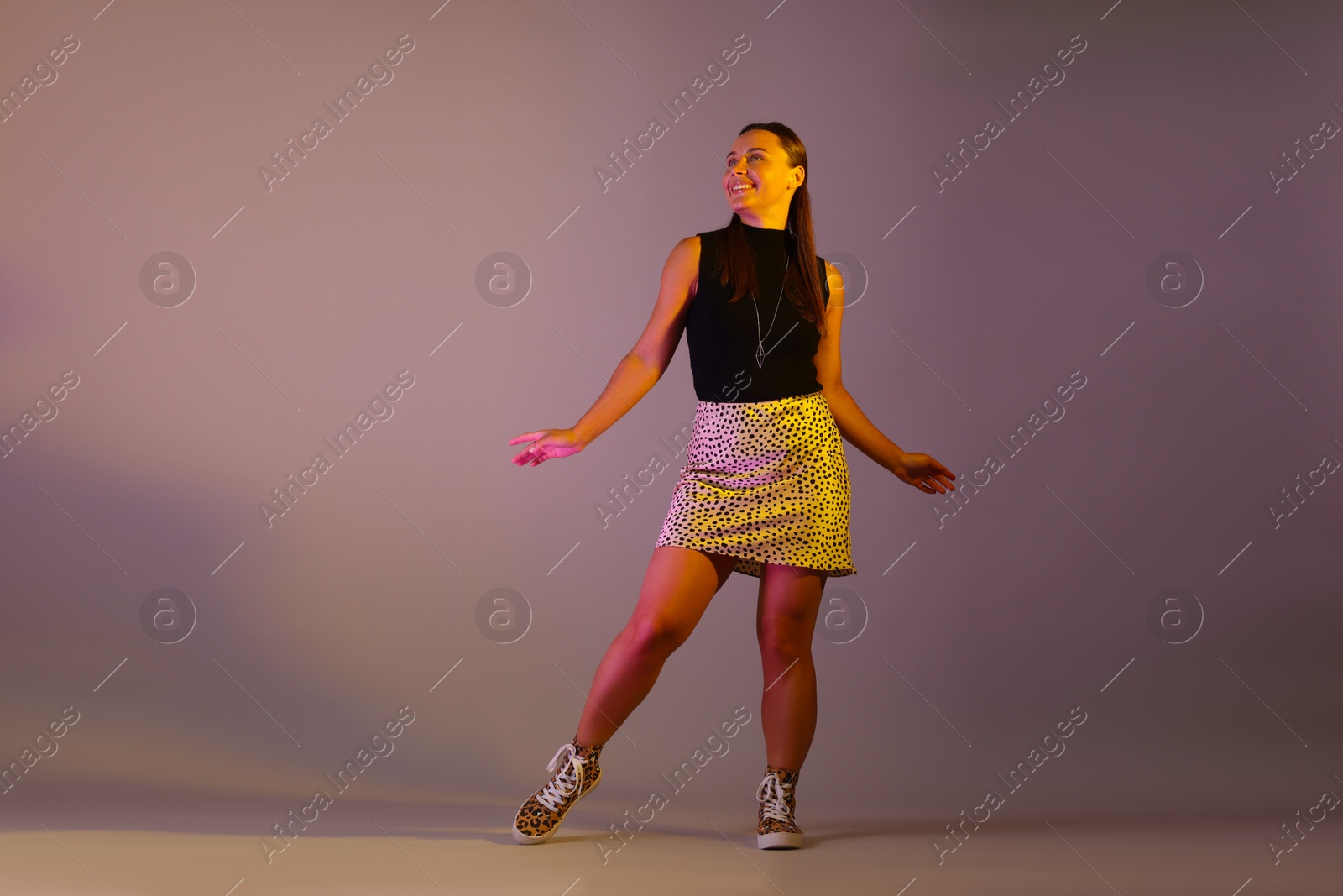 Photo of Smiling woman in neon lights against grey background, low angle view
