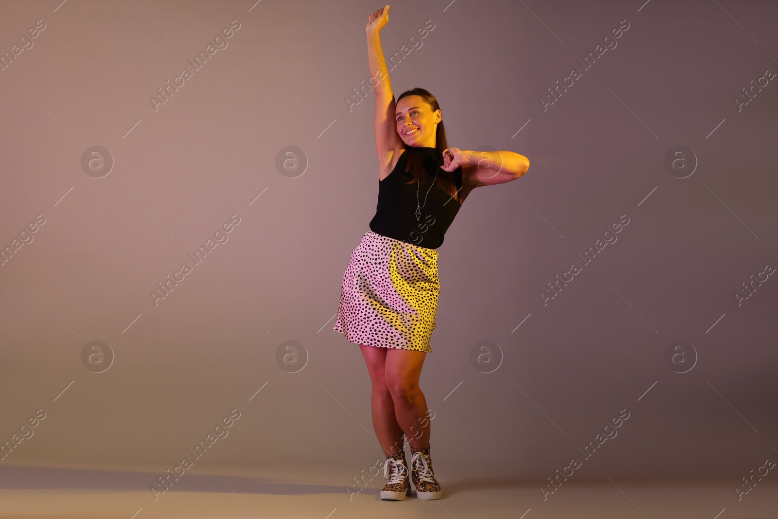 Smiling woman dancing in neon lights against grey background Photo of Smiling woman dancing in neon lights against grey background
