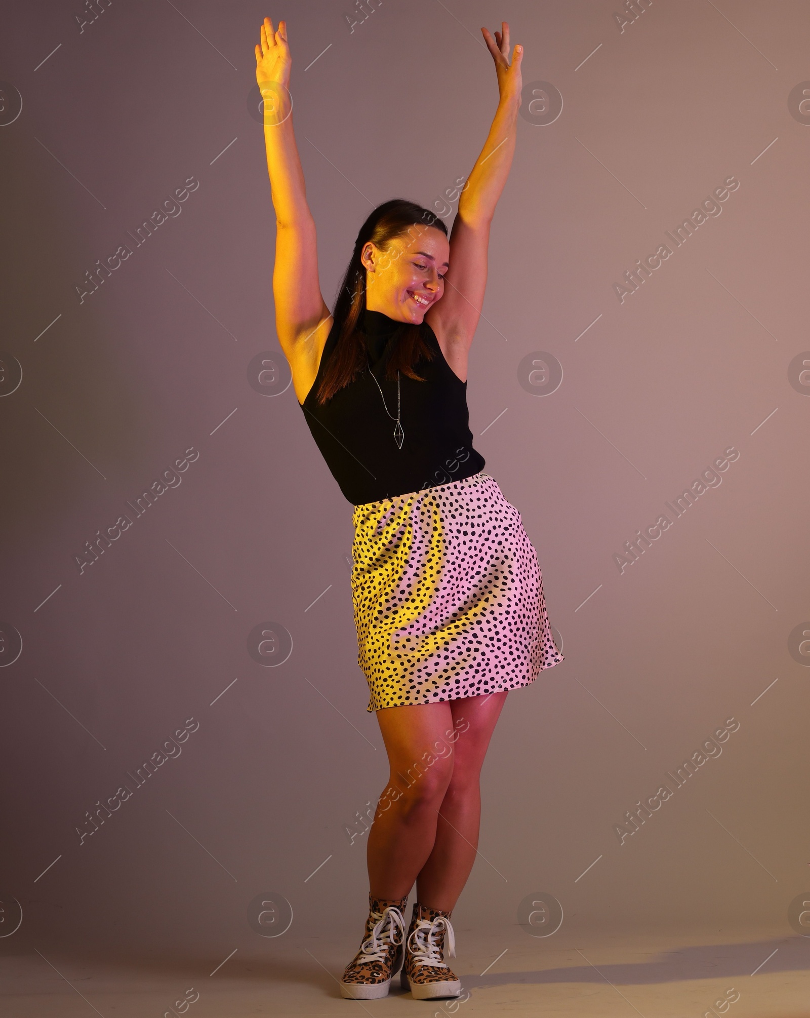 Smiling woman dancing in neon lights against grey background Photo of Smiling woman dancing in neon lights against grey background