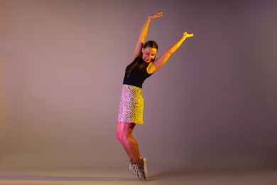 Photo of Smiling woman dancing in neon lights against grey background