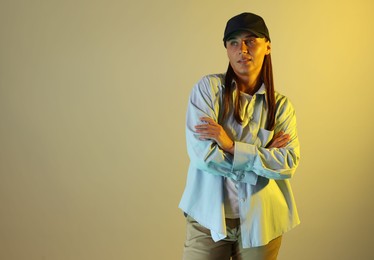 Photo of Beautiful woman wearing baseball cap with crossed arms in neon lights against color background. Space for text