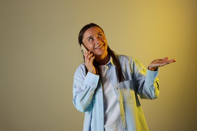 Photo of Smiling woman talking by smartphone in neon lights against color background. Space for text