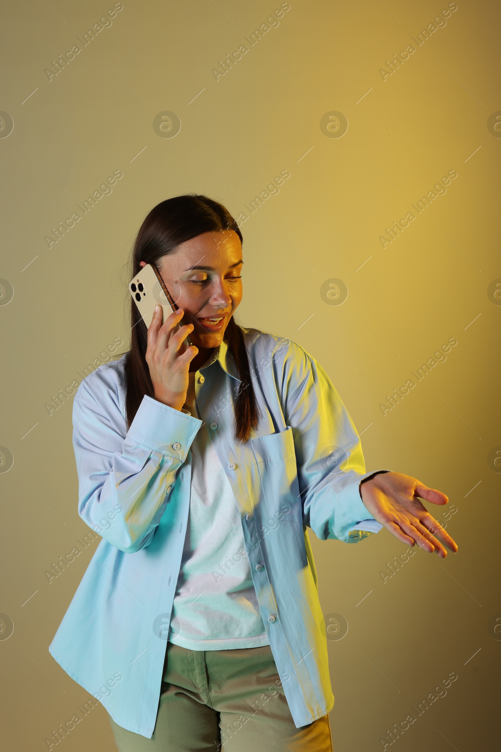 Beautiful woman talking by smartphone in neon lights against color background Photo of Beautiful woman talking by smartphone in neon lights against color background