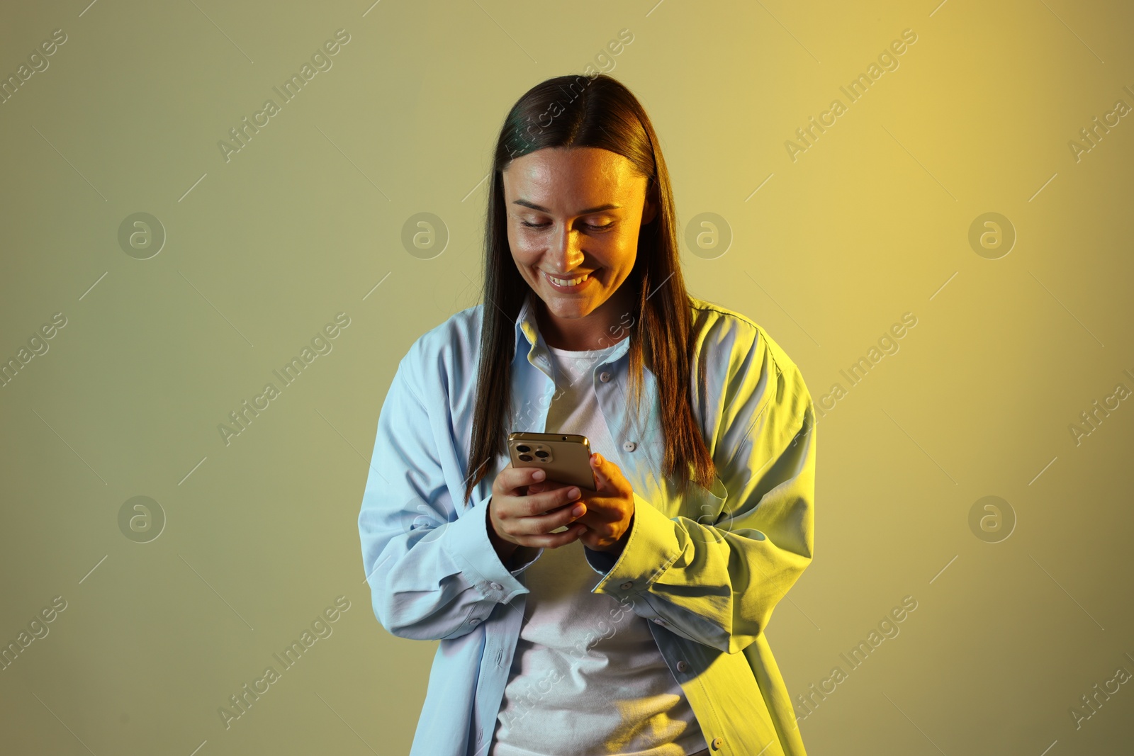 Smiling woman using smartphone in neon lights against color background Photo of Smiling woman using smartphone in neon lights against color background