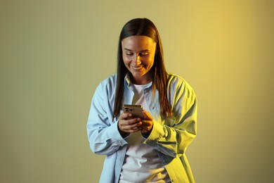 Photo of Smiling woman using smartphone in neon lights against color background