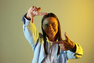 Photo of Smiling woman showing frame gesture in neon lights against color background