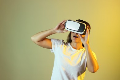 Photo of Emotional woman using virtual reality headset in neon lights against color background