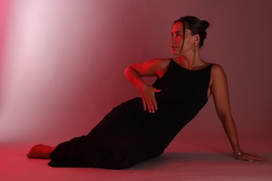 Photo of Beautiful woman wearing dress posing in neon lights against red background
