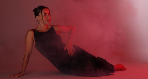 Photo of Beautiful woman wearing dress posing in neon lights and smoke against red background