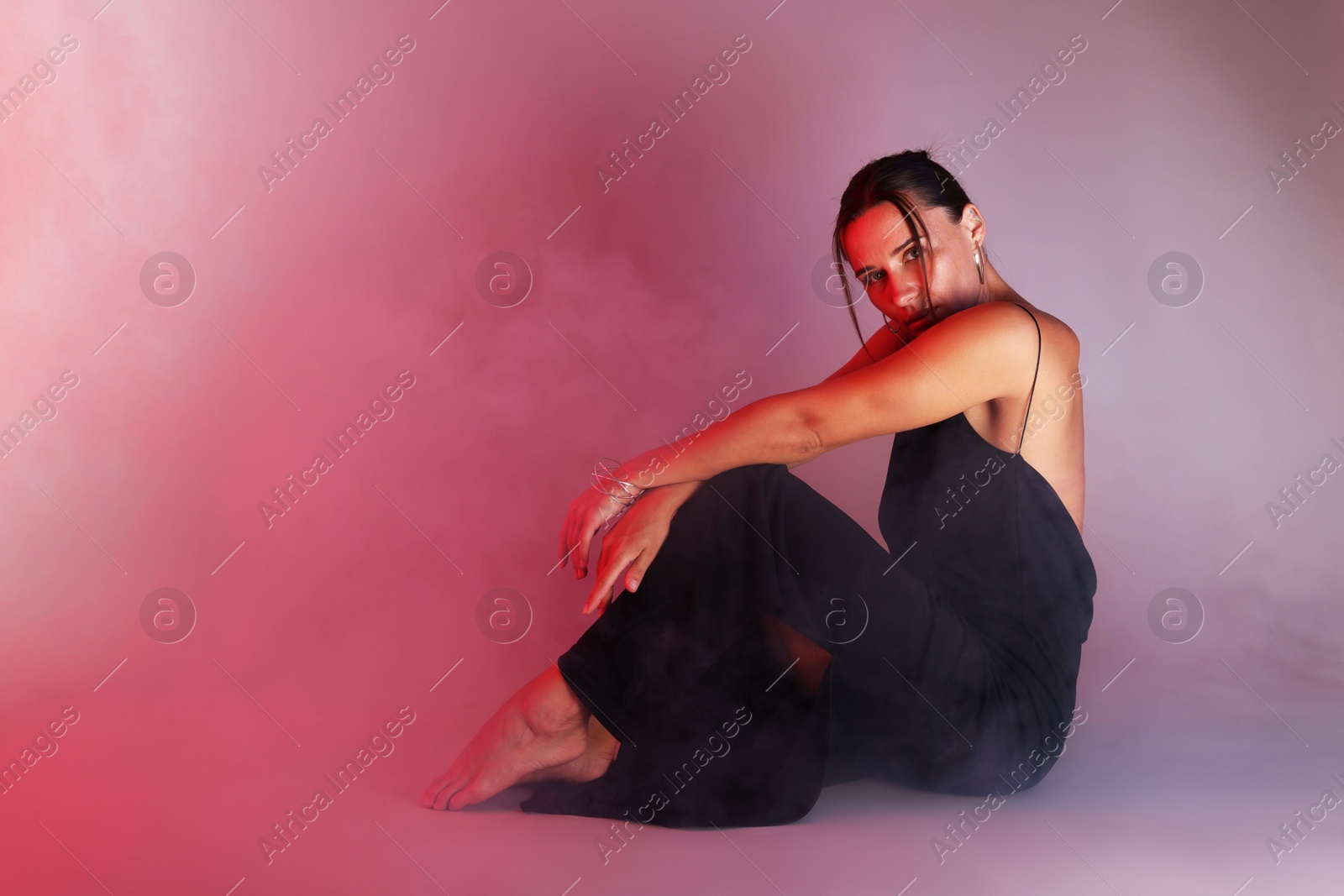 Beautiful woman wearing dress posing in neon lights and smoke against color background. Space for text Photo of Beautiful woman wearing dress posing in neon lights and smoke against color background. Space for text