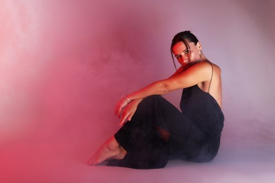 Photo of Beautiful woman wearing dress posing in neon lights and smoke against color background. Space for text