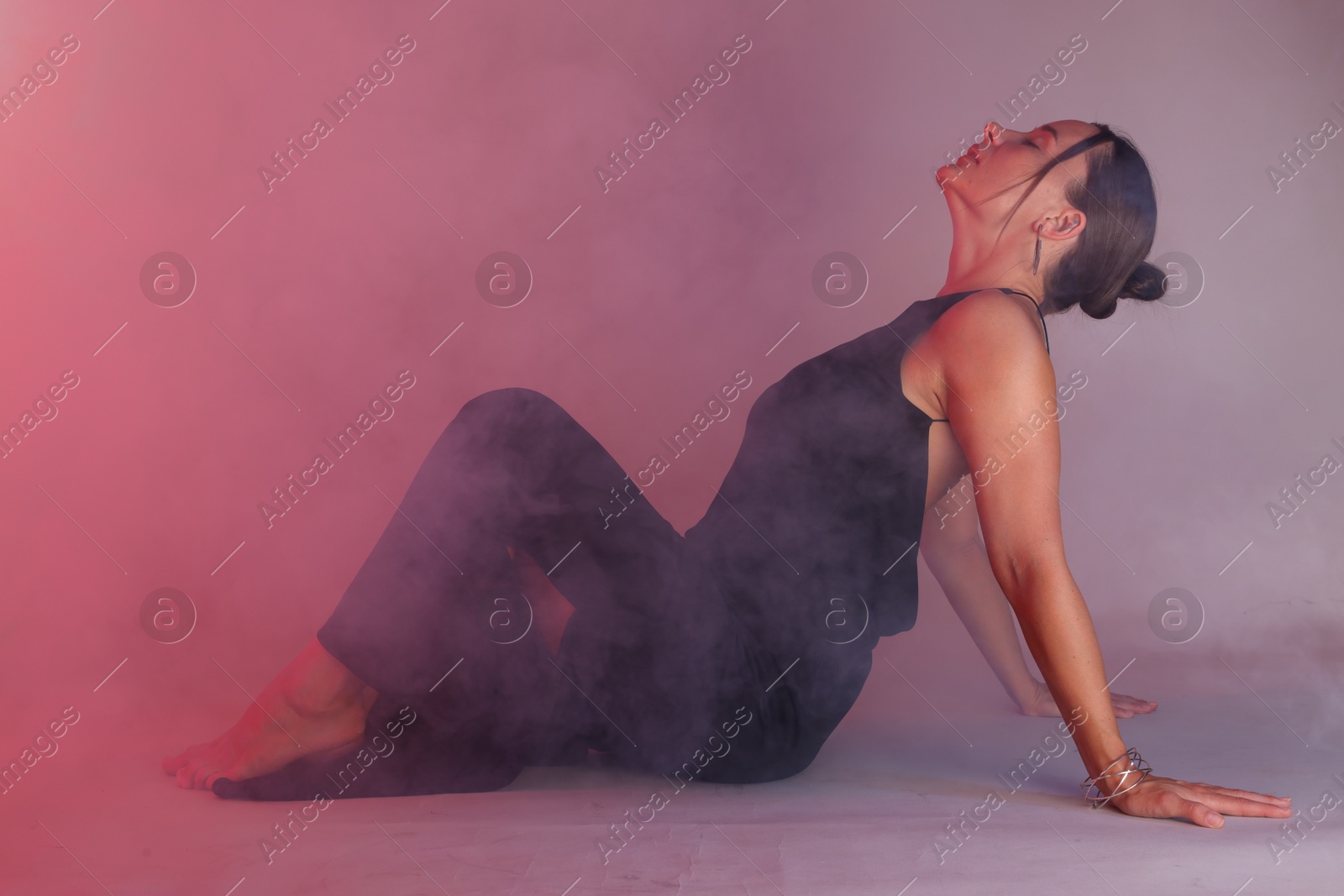 Beautiful woman wearing dress posing in neon lights and smoke against color background Photo of Beautiful woman wearing dress posing in neon lights and smoke against color background