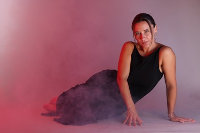 Photo of Beautiful woman wearing dress posing in neon lights and smoke against color background