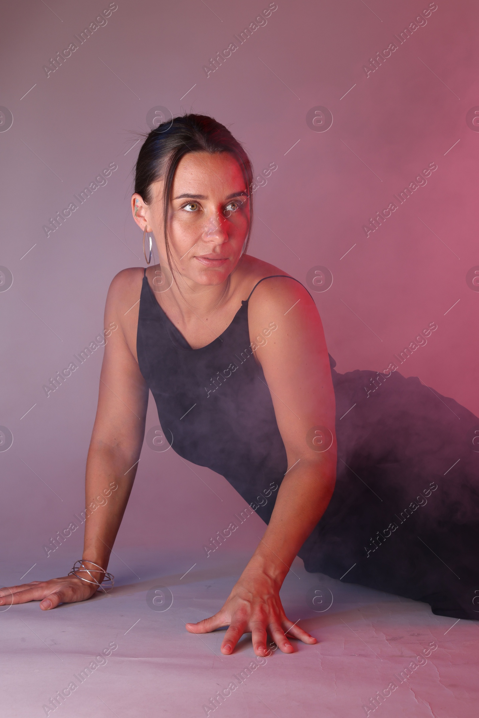 Beautiful woman wearing dress posing in neon lights and smoke against color background Photo of Beautiful woman wearing dress posing in neon lights and smoke against color background